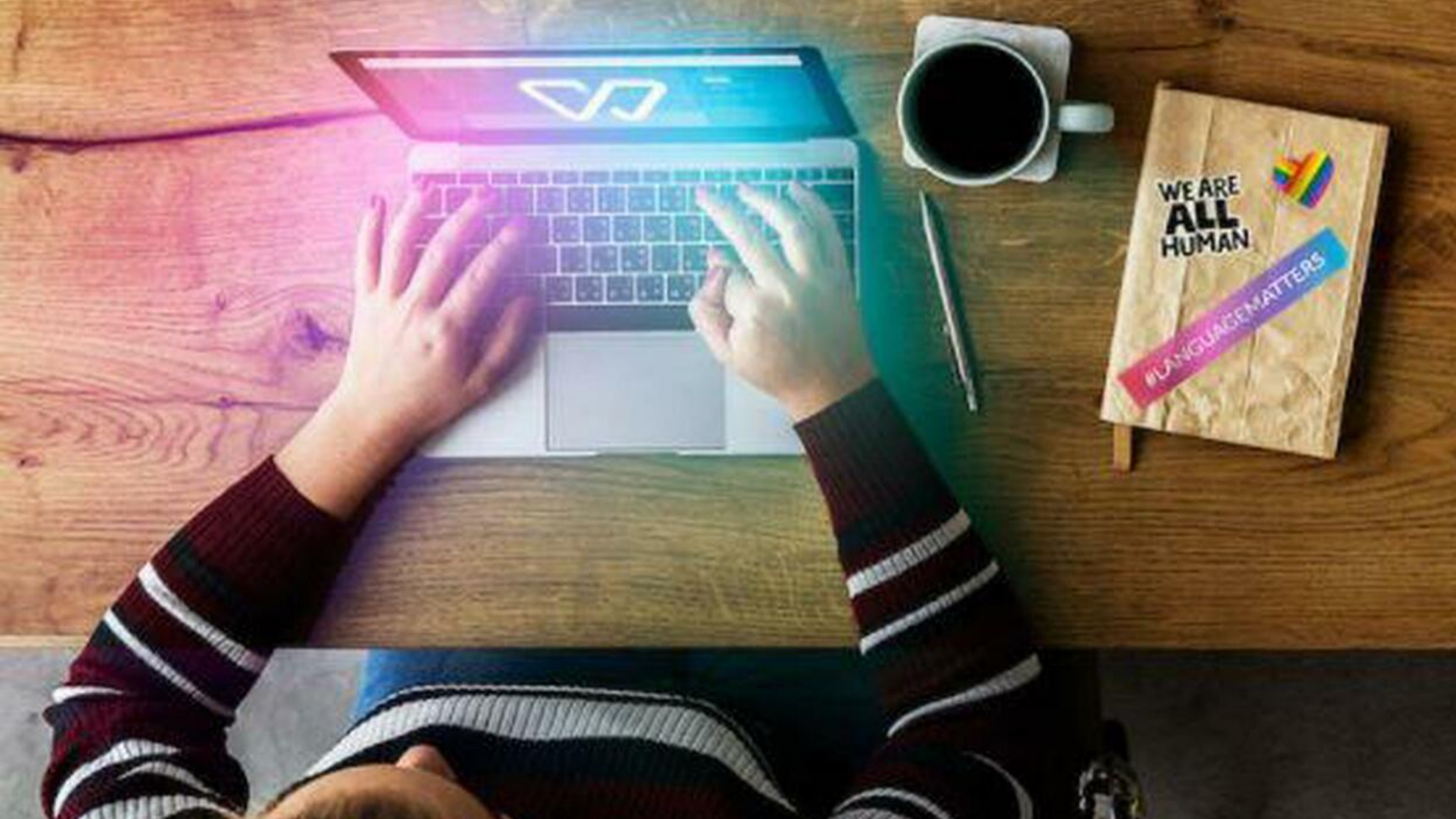 Woman writing on a laptop, with a a coffee and a notebook next to her