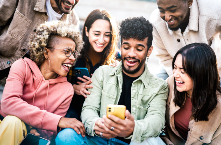 A groupe of young people laughing and looking at a cell phone