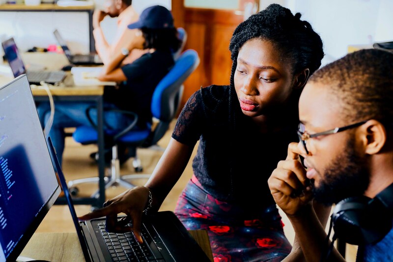 A team member guiding another on a computer, showcasing peer-to-peer learning in a tech workspace.