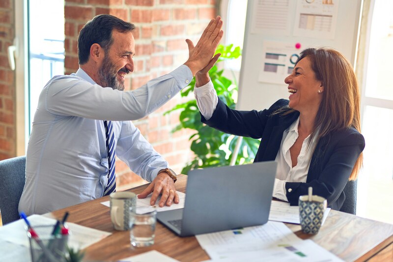 Two professionals celebrating with a high-five in an office, representing successful collaboration.