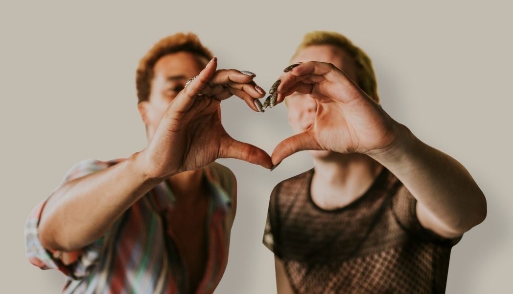 Two non-binary people forming a heart with their hands.