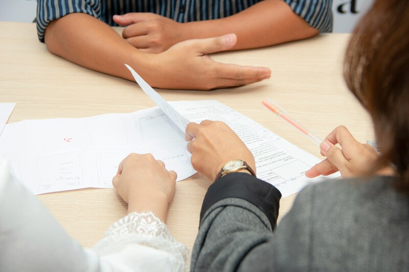 Two individuals discussing documents on a table, indicating a collaborative work environment.